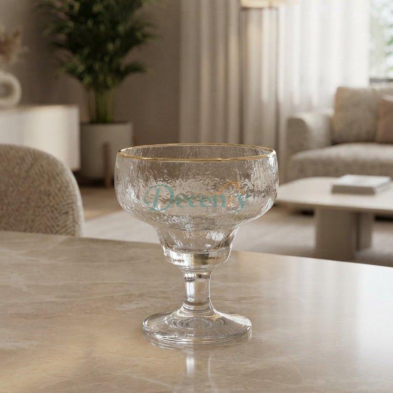 A single hammered glass ice cream cup with a delicate gold rim sitting on a marble table in a bright modern living room.