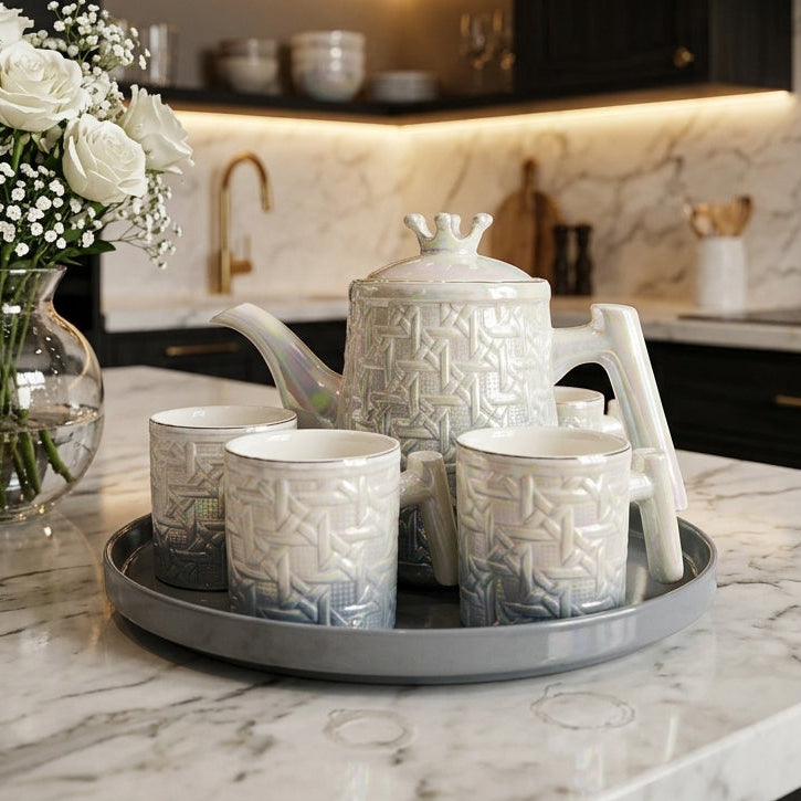 8 piece iridescent pearl ceramic revolving tea set with teapot, cups, and rotating tray placed on a marble kitchen island beside a vase of white roses.