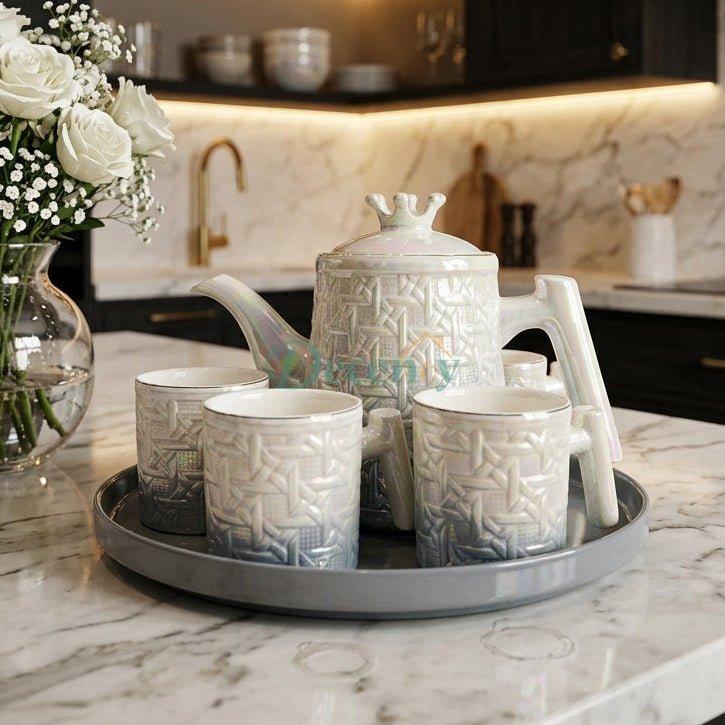 8 piece iridescent pearl ceramic revolving tea set with teapot, cups, and rotating tray placed on a marble kitchen island beside a vase of white roses.