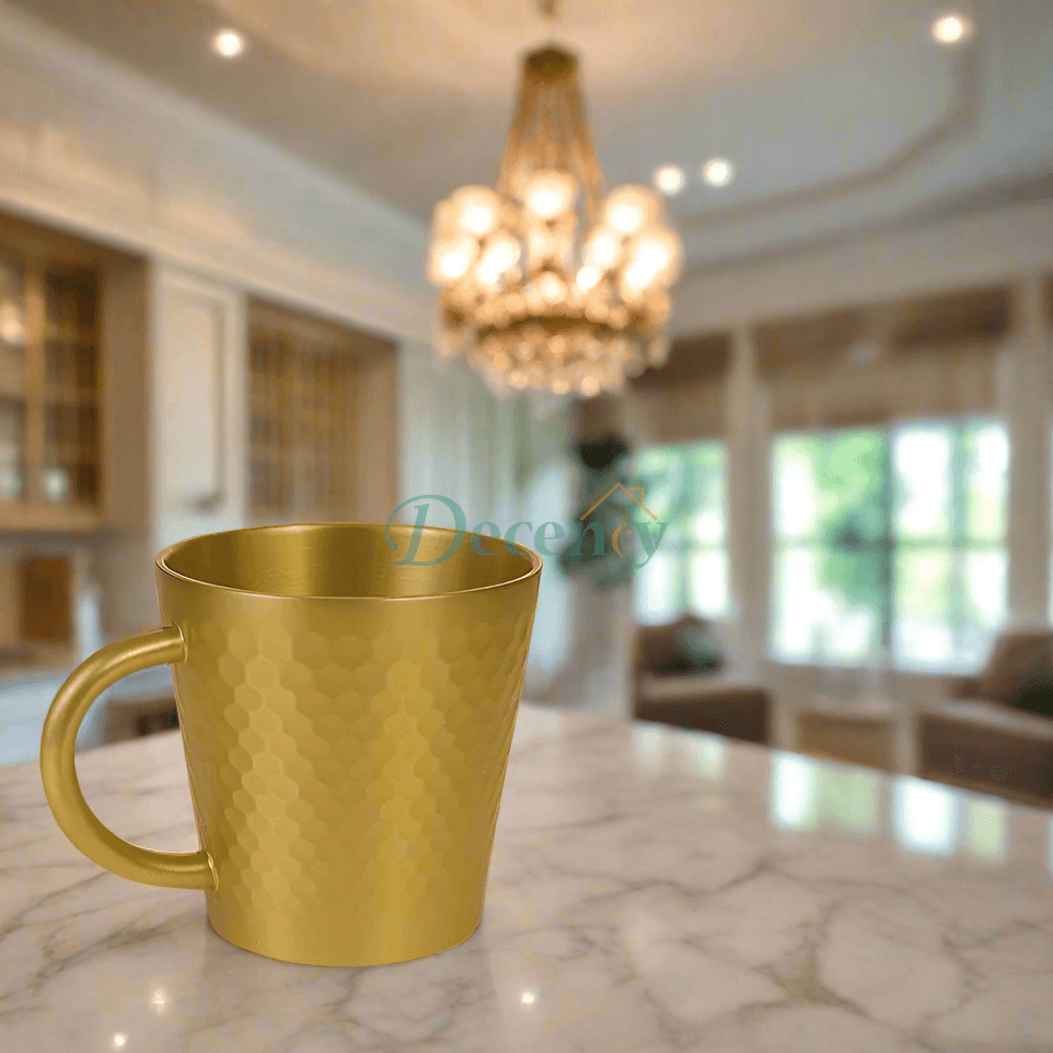Gold mug on a marble countertop in a kitchen with a chandelier.