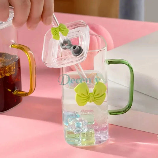 Clear water bottle with green handles and bows on a pink surface