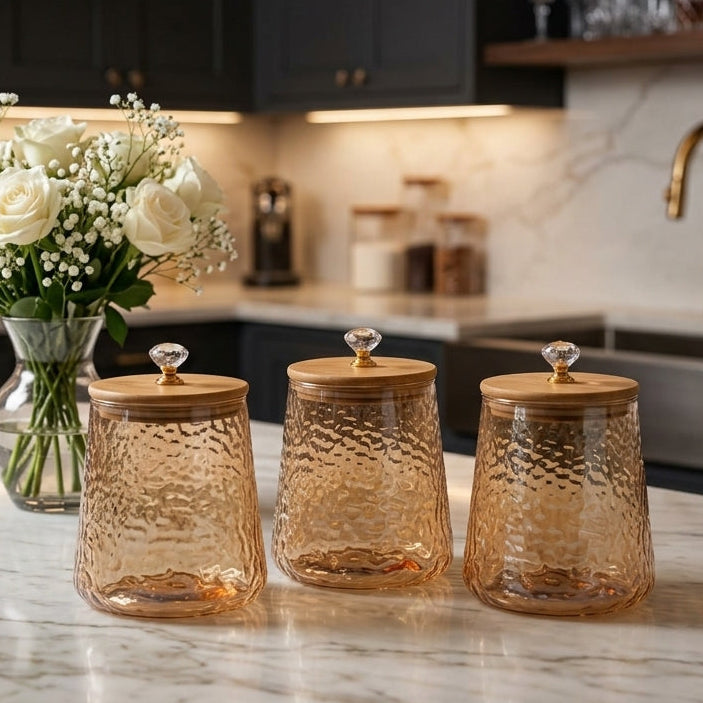 Set of 3 amber hammered glass jars with bamboo wooden lids and crystal knobs on a marble kitchen counter