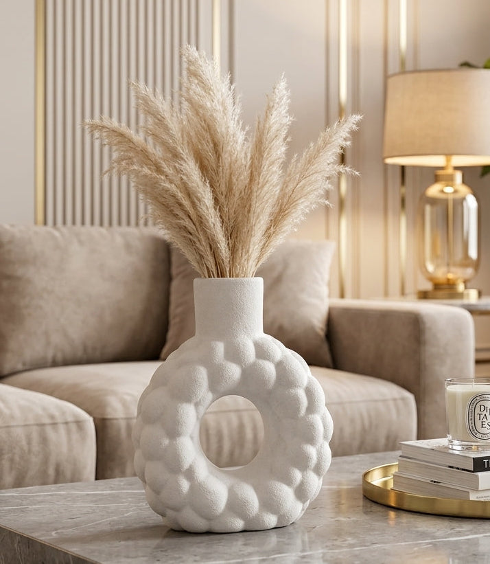 White ceramic donut flower vase styled with fluffy pampas grass on a marble coffee table.