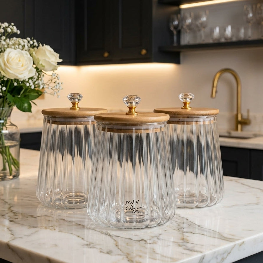 Set of three clear fluted glass jars with wooden lids and gold crystal knobs on a marble kitchen counter