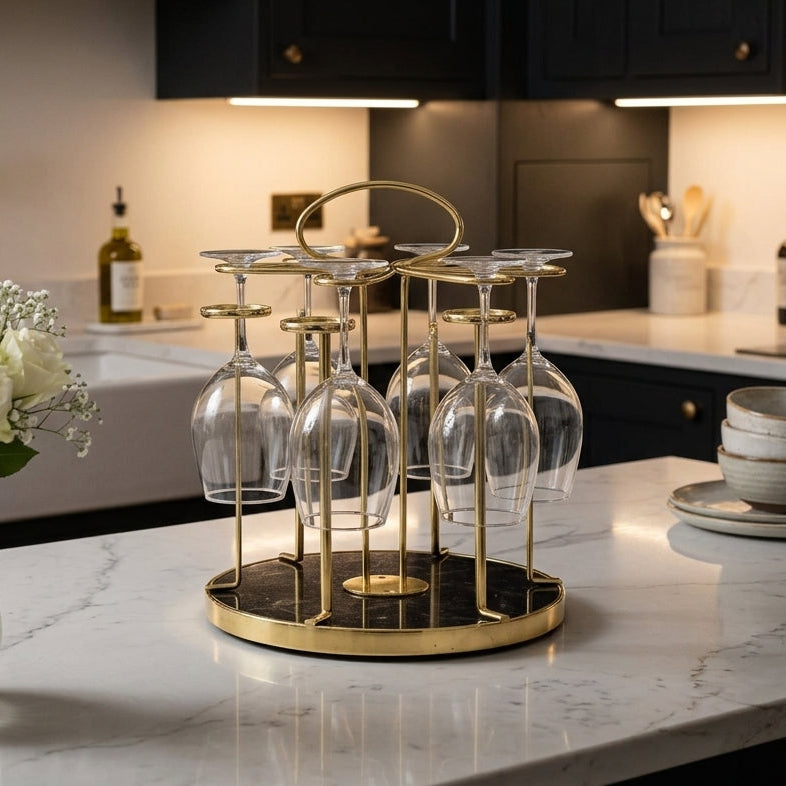 Luxury gold metallic glassware stand with a round black marble base holding stemware on a marble kitchen counter.