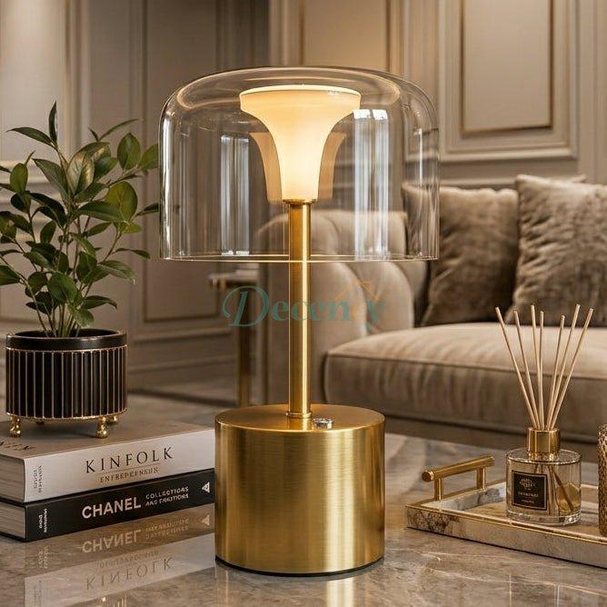 Cordless gold table light with transparent glass shade glowing softly in a living room