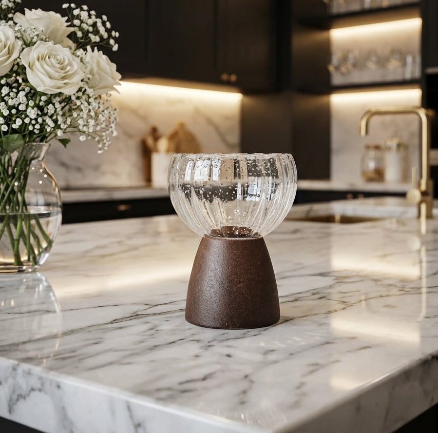 Ribbed glass candle holder with brown ceramic base placed on a marble kitchen island counter