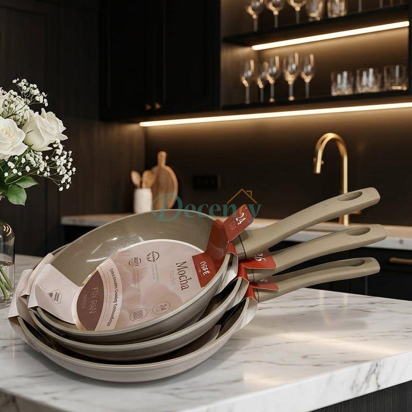 Stack of OSFE Mocha non-stick ceramic frypans on a marble kitchen countertop.