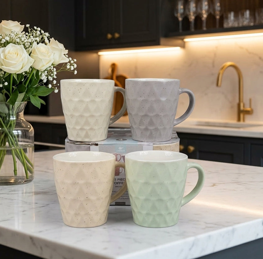 Set of 4 pastel-colored textured ceramic tea and coffee mugs displayed on a white marble kitchen counter next to white flowers..