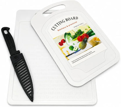 A white plastic cutting board with a built-in black grater insert and a matching black-handled knife, shown on a clean white background. The top of the board features a printed insert with the text 'CUTTING BOARD' and a colorful photo of fresh vegetables.