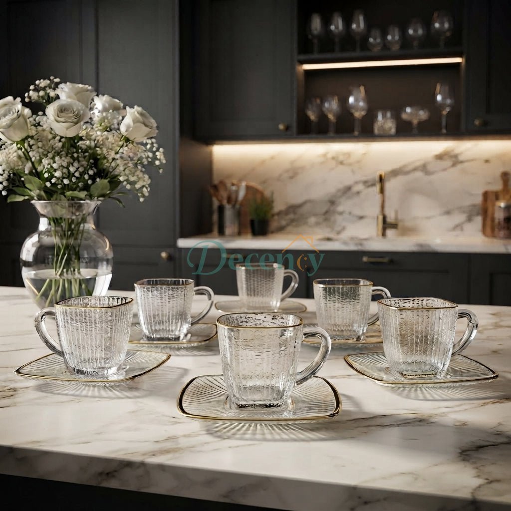 Six pieces of textured glass cups and saucers with gold rims arranged on a marble kitchen counter.
