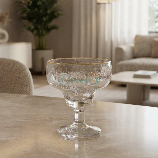 A single hammered glass ice cream cup with a delicate gold rim sitting on a marble table in a bright modern living room.   