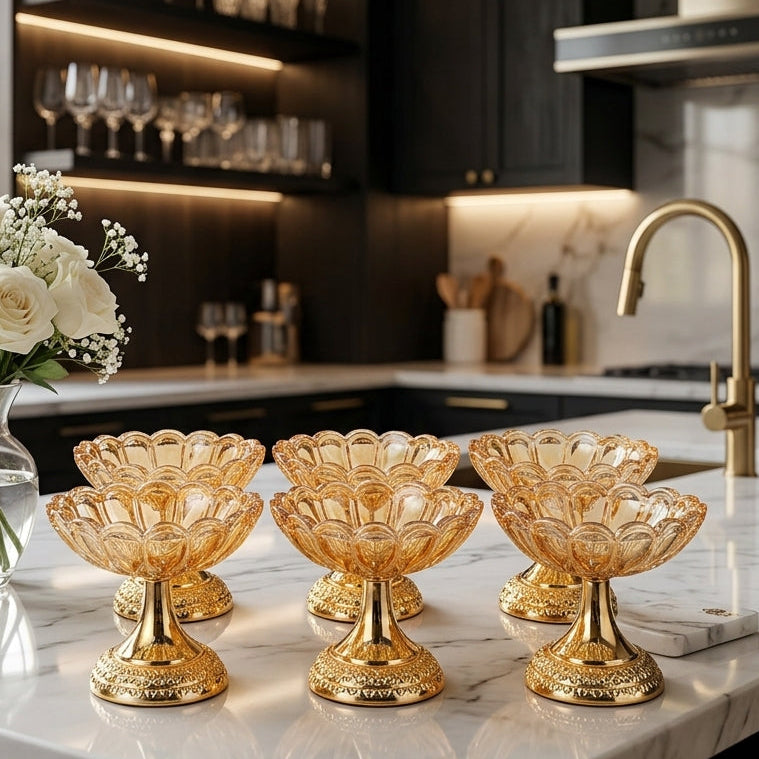 Set of 6 amber glass dessert bowls with gold pedestals on a kitchen marble countertop next to white flowers