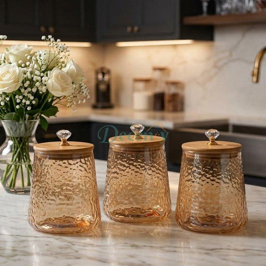 Set of 3 amber hammered glass jars with bamboo wooden lids and crystal knobs on a marble kitchen counter