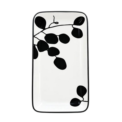 Top-down view of a rectangular ceramic serving tray featuring a black leaf and branch pattern on a white background.   