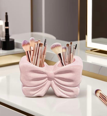 Pink and white bow-shaped makeup brush holders displayed on a glass vanity shelf