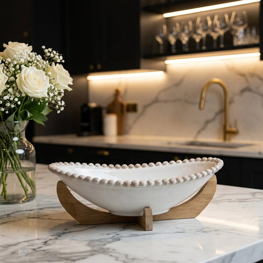 White ceramic boat shape fruit bowl with beaded rim placed on a wooden stand