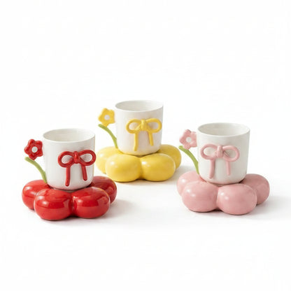 Three cute ceramic coffee mugs with bow details resting on colorful flower-shaped coaster saucers.