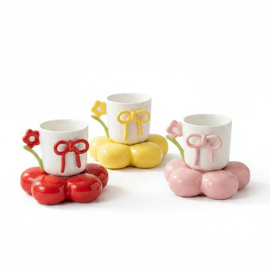 Three cute ceramic coffee mugs with bow details resting on colorful flower-shaped coaster saucers.