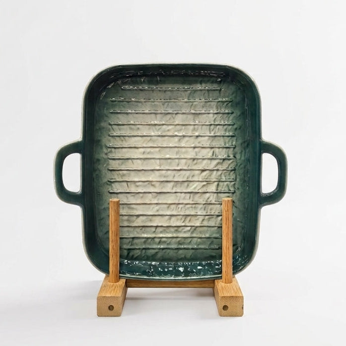 Green ceramic rectangular grill pan resting on a wooden display stand.   