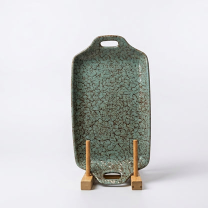 Turquoise crackle glazed ceramic serving tray standing upright on a wooden display holder. 