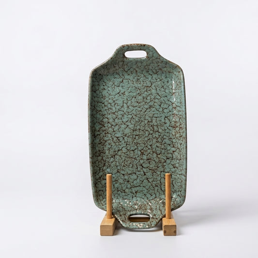 Turquoise crackle glazed ceramic serving tray standing upright on a wooden display holder. 