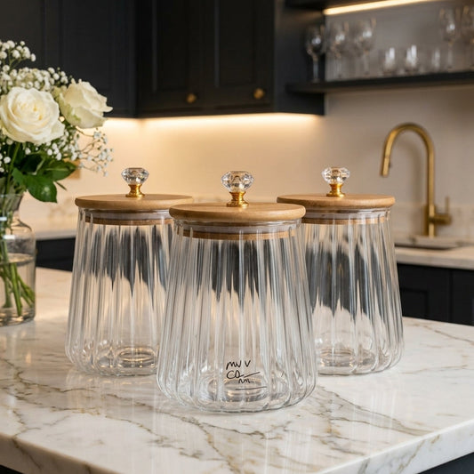 Set of three clear fluted glass jars with wooden lids and gold crystal knobs on a marble kitchen counter