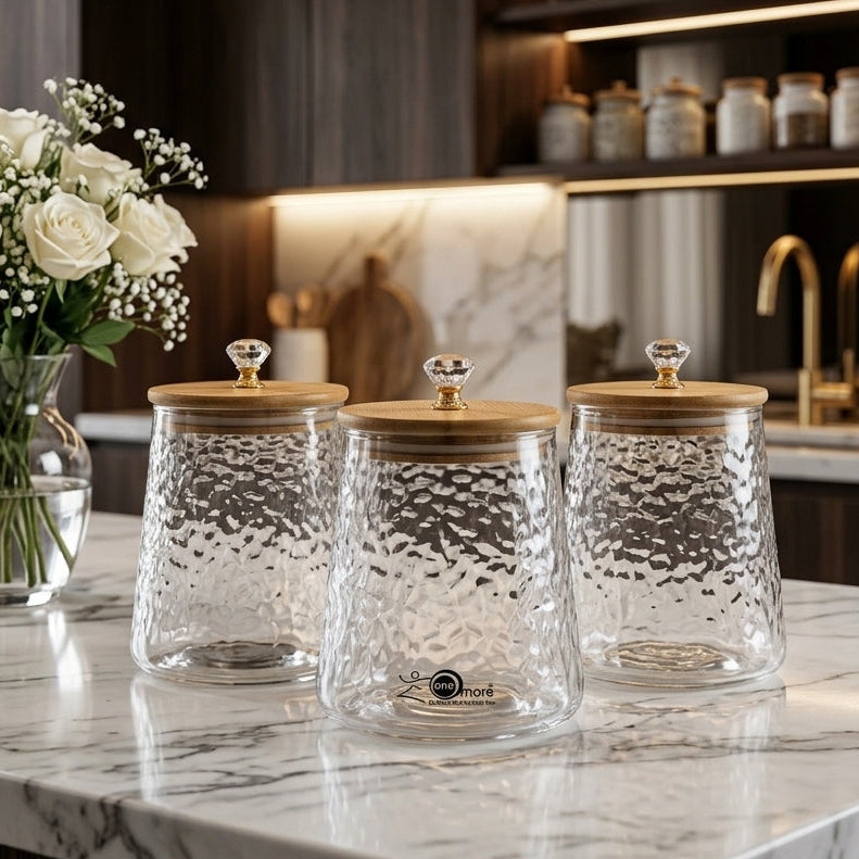 Set of 3 clear hammer-textured glass spice jars with wooden lids and crystal knobs on a marble kitchen island