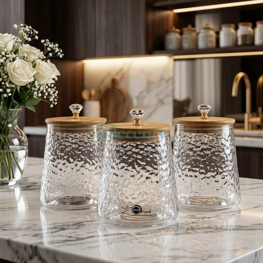 Set of 3 clear hammer-textured glass spice jars with wooden lids and crystal knobs on a marble kitchen island