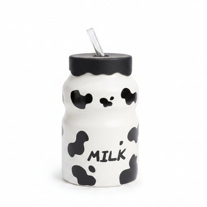 Front view of white cow print glass milk bottle with black lid and glass str