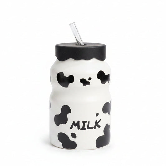 Front view of white cow print glass milk bottle with black lid and glass str