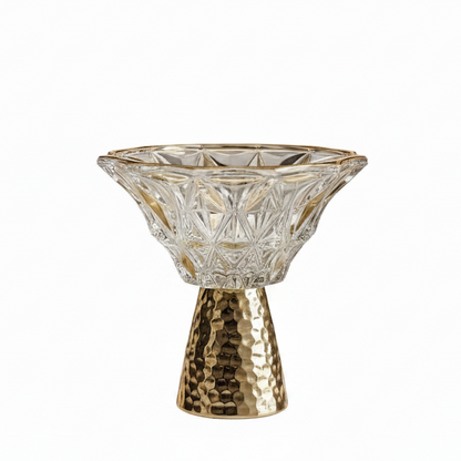 Clear cut-glass pedestal bowl with gold rim sitting on a hammered gold stand on a marble countertop.