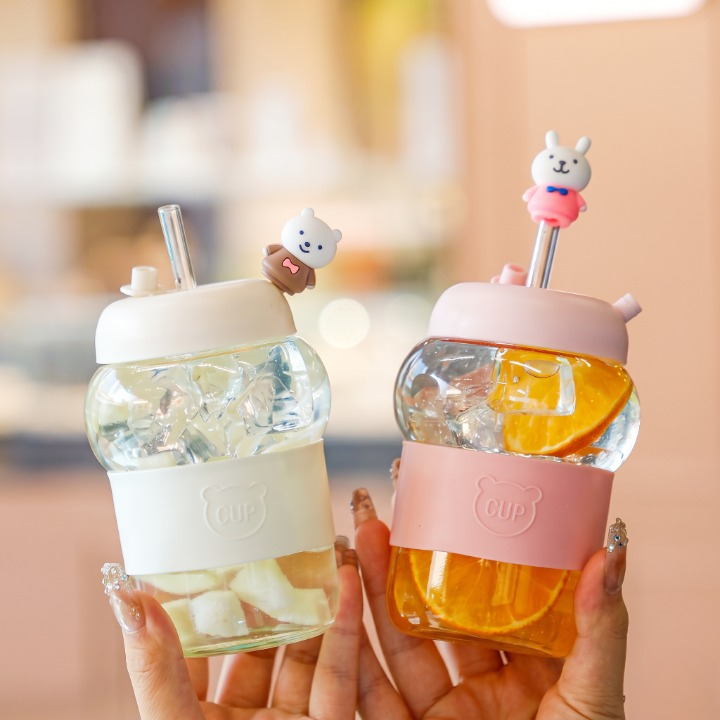 Hand holding a clear 400ml cute 3d bear glass drinking bottle filled with iced tea and fitted with a glass straw