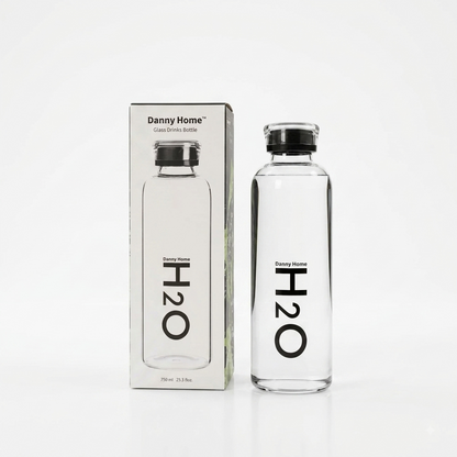 Danny Home 750ml clear glass water bottle with black H2O print next to its original box on a marble countertop.