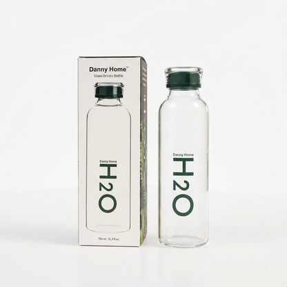 Danny Home 750ml clear glass water bottle with green H2O logo standing next to its original packaging on a kitchen marble counter.