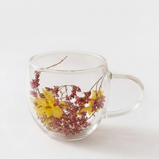 Double wall clear glass coffee mug with pink dried flower petals inside on a woven coaster