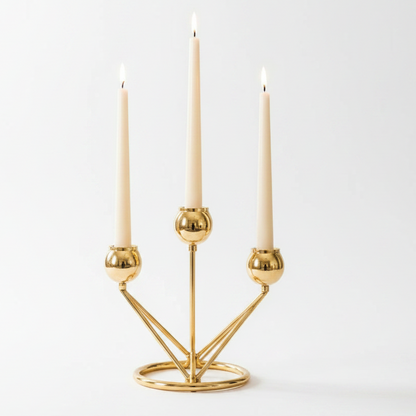 Elegant gold metal candelabra holding three white taper candles on a polished table surface