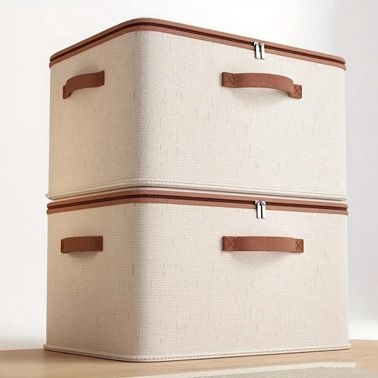 Two stacked beige fabric clothes storage boxes with brown zippers and handles on a wooden table