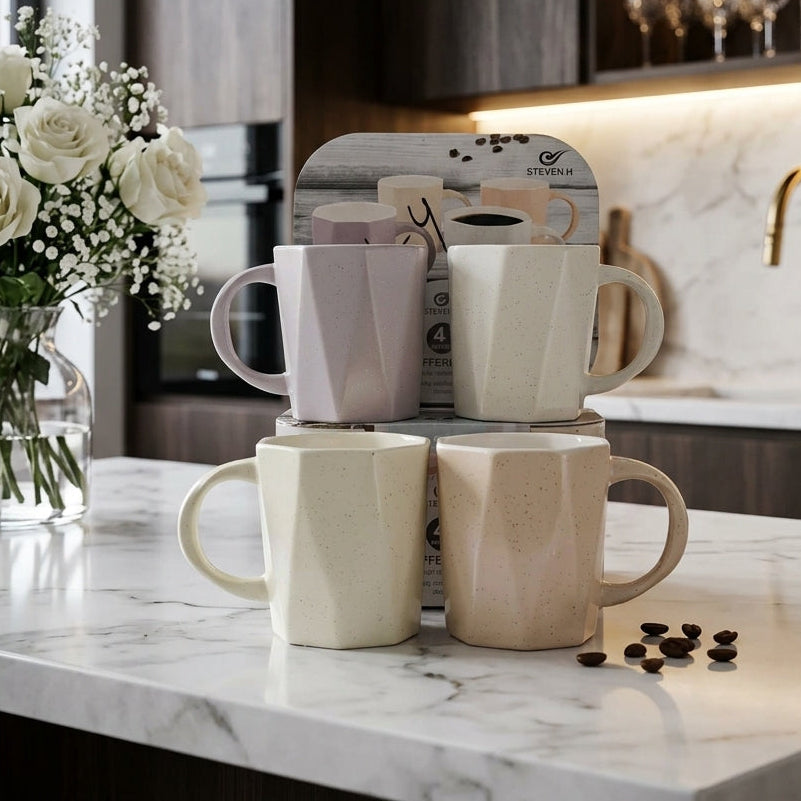 Set of four geometric ceramic coffee mugs in neutral pastel colors displayed on a marble kitchen counter