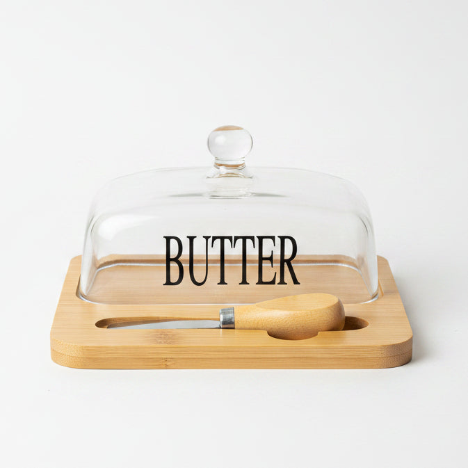 Clear glass butter dish printed with BUTTER text on wooden tray with spreader knife