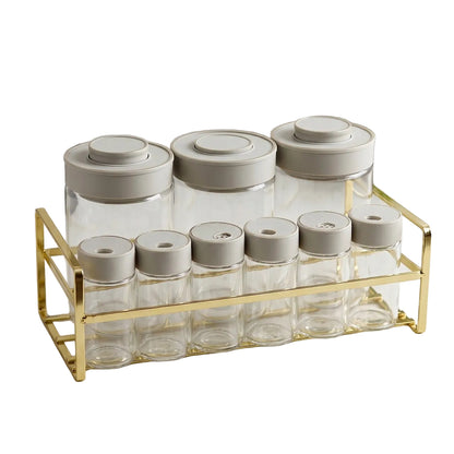 Luxury 9-piece glass spice jar set with gold wire stand on a marble kitchen countertop.
