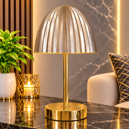 A modern table lamp with a ribbed dome shade and a polished gold base, shown lit on a dark marble table in a styled interior setting.