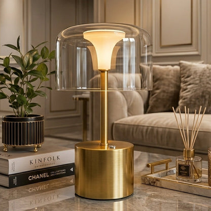 Cordless gold table light with transparent glass shade glowing softly in a living room