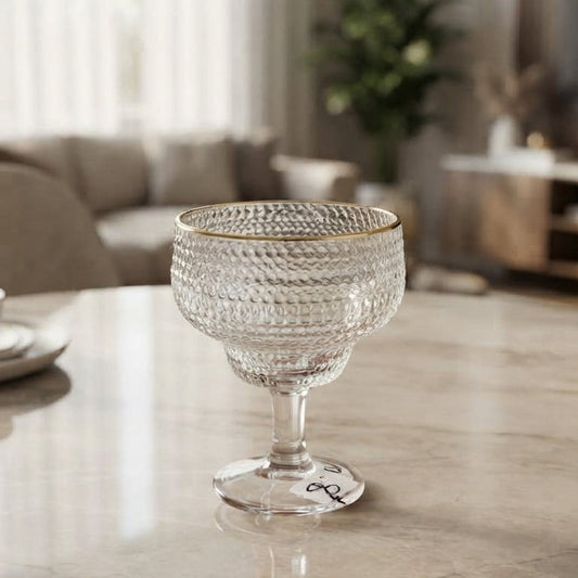 Single textured glass dessert bowl with a shiny gold rim placed elegantly on a polished marble dining table in a bright room. 