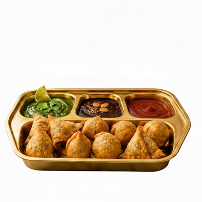 Gold stainless steel 4-compartment serving tray filled with crispy samosas, mint chutney, imli chutney, and ketchup.