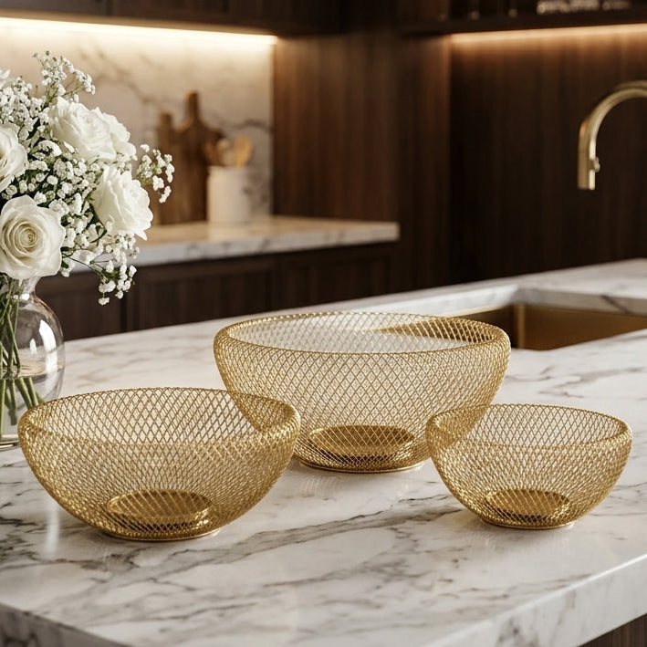 Three-piece luxury gold wire mesh fruit bowl set displayed on a white marble kitchen counter.