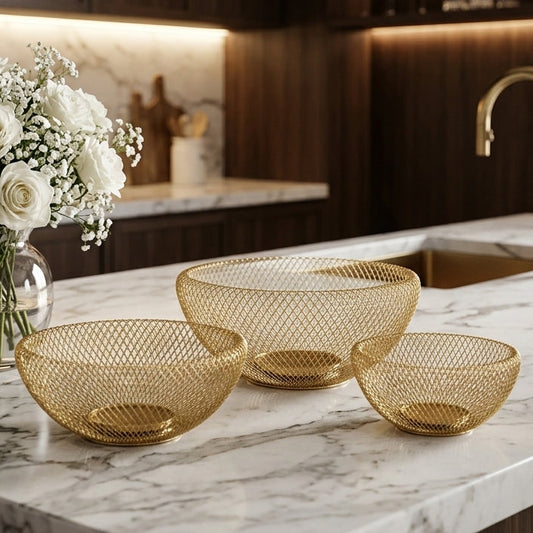 Three-piece luxury gold wire mesh fruit bowl set displayed on a white marble kitchen counter.