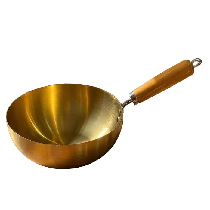 Golden mini saucepan with smooth wooden handle placed on a wooden kitchen table.