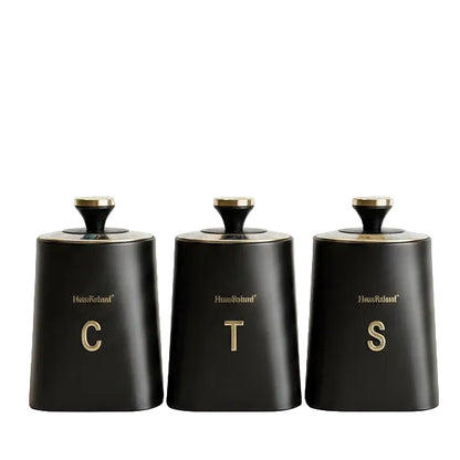 Haus Roland black matte 3 piece canister set with gold lettering for tea coffee and sugar on marble countertop