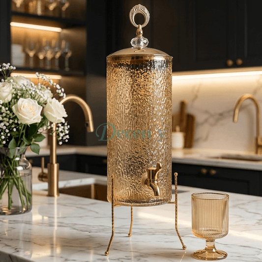 Luxury amber textured glass beverage dispenser on a gold metal tripod stand in a modern kitchen setup.